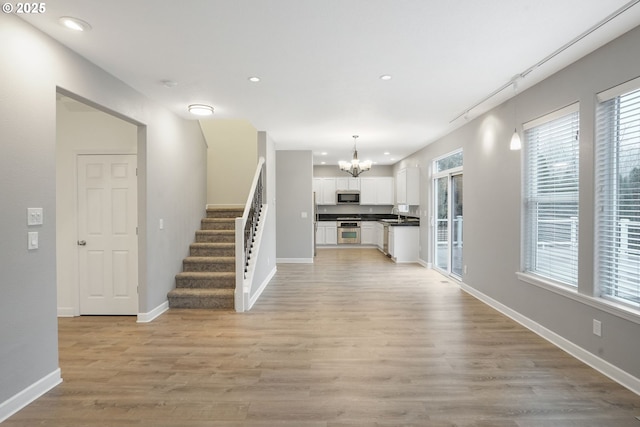 unfurnished living room featuring a notable chandelier and light wood-type flooring