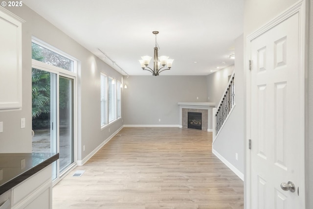 unfurnished living room with a notable chandelier, light wood-type flooring, and a fireplace