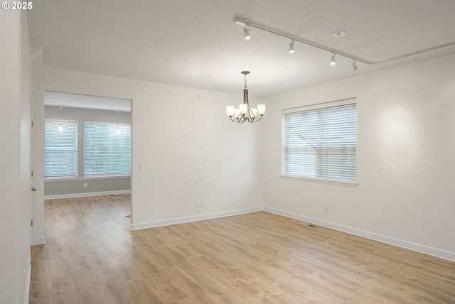 empty room with an inviting chandelier, plenty of natural light, track lighting, and light wood-type flooring