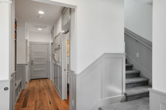 corridor with a decorative wall, a wainscoted wall, light wood-type flooring, stairs, and recessed lighting