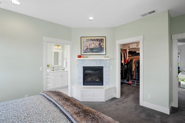 carpeted bedroom featuring a walk in closet, a tiled fireplace, a closet, a sink, and recessed lighting