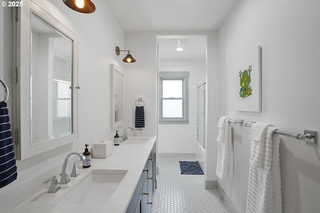bathroom featuring double vanity, shower / bath combination with glass door, and baseboards
