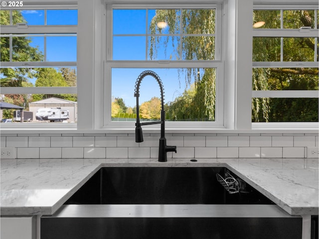 room details featuring decorative backsplash, sink, and light stone counters