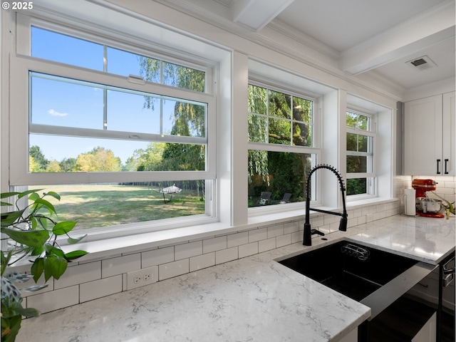 kitchen with light stone counters, sink, white cabinetry, and beamed ceiling