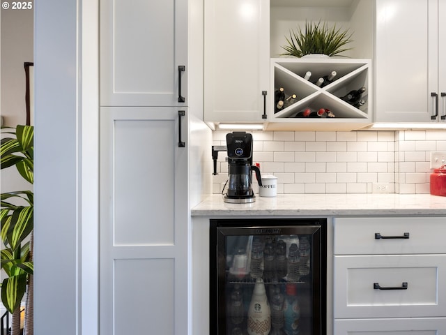 bar with decorative backsplash, white cabinets, beverage cooler, and light stone countertops