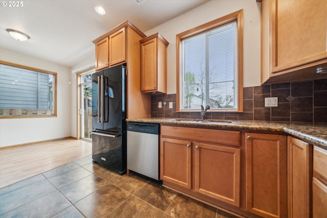 kitchen featuring a wealth of natural light, high end black refrigerator, dishwasher, and a sink