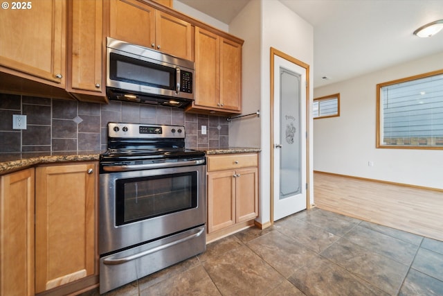 kitchen with tasteful backsplash, baseboards, dark stone counters, and appliances with stainless steel finishes