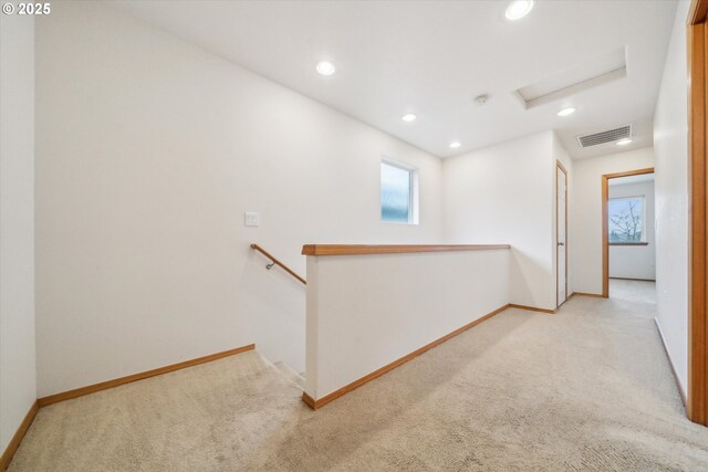 hall with visible vents, an upstairs landing, attic access, and light carpet