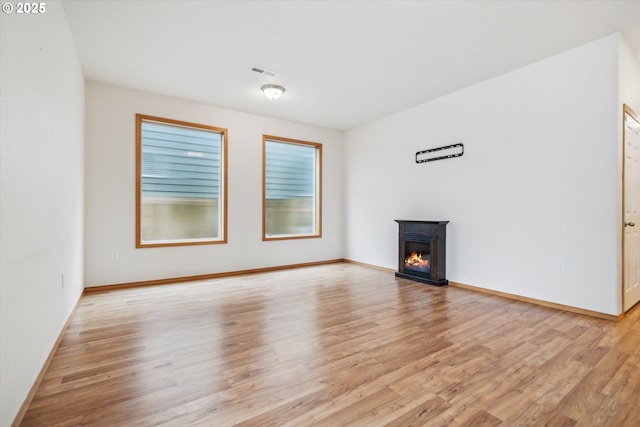 unfurnished living room with light wood-type flooring, baseboards, a glass covered fireplace, and visible vents