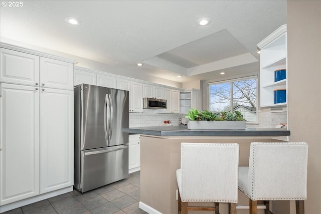 kitchen featuring white cabinets, a kitchen breakfast bar, light tile patterned floors, a tray ceiling, and stainless steel appliances