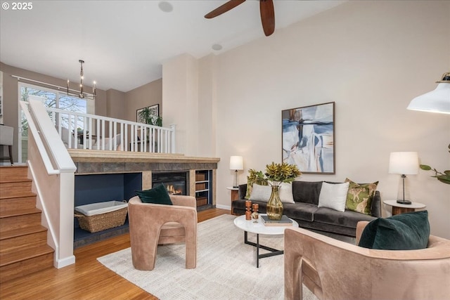 living room with a tiled fireplace, ceiling fan with notable chandelier, and wood-type flooring