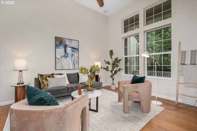 living room featuring ceiling fan, a towering ceiling, and light hardwood / wood-style flooring