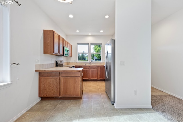kitchen with appliances with stainless steel finishes, a sink, recessed lighting, light countertops, and brown cabinetry