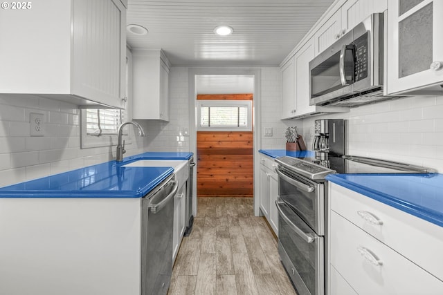 kitchen with light wood-type flooring, white cabinetry, backsplash, stainless steel appliances, and a sink