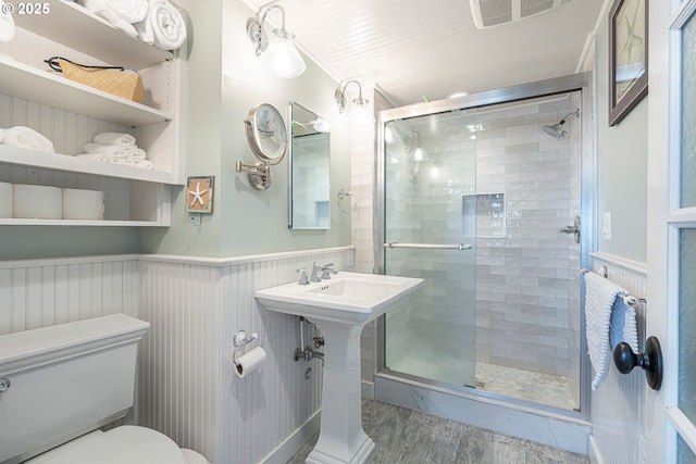 full bathroom with toilet, a wainscoted wall, a stall shower, and wood finished floors