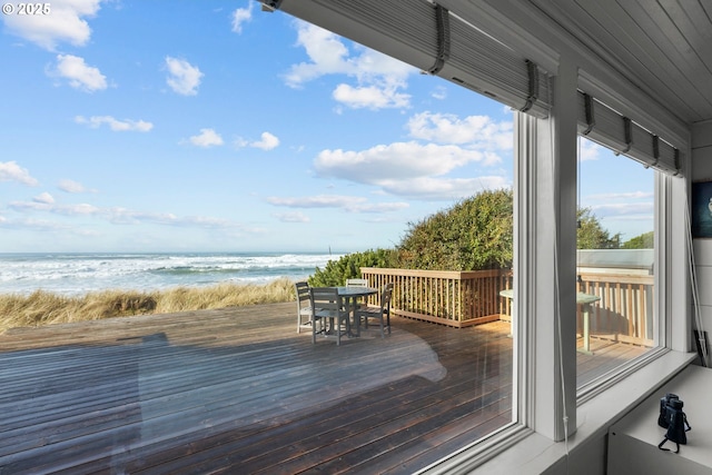 wooden terrace featuring a water view, outdoor dining area, and a view of the beach