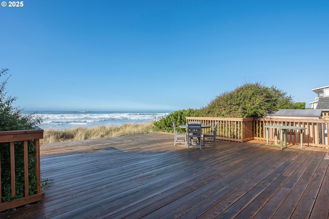 wooden terrace featuring a water view, outdoor dining space, and a view of the beach