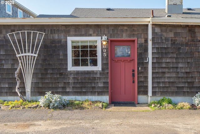 entrance to property featuring a shingled roof and a chimney