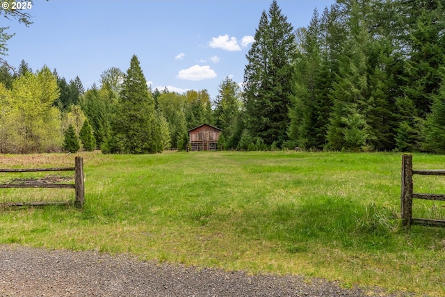 view of yard with a wooded view, fence, and a rural view