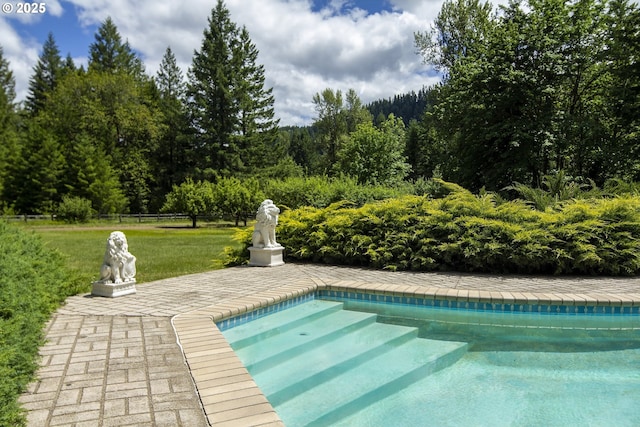outdoor pool with a yard, a forest view, and fence