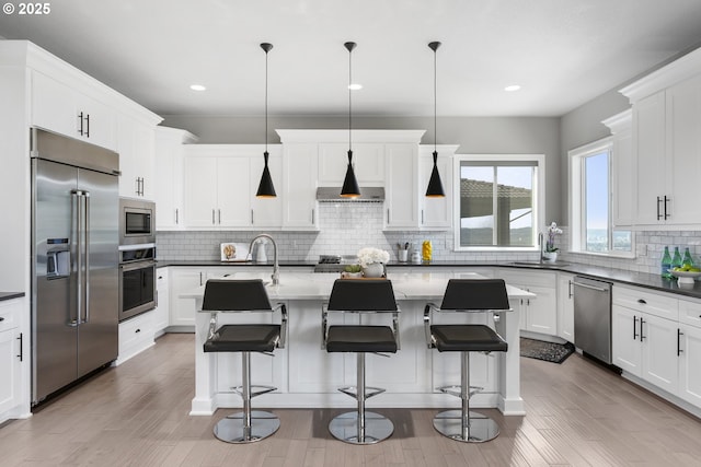 kitchen with recessed lighting, an island with sink, a sink, tasteful backsplash, and built in appliances
