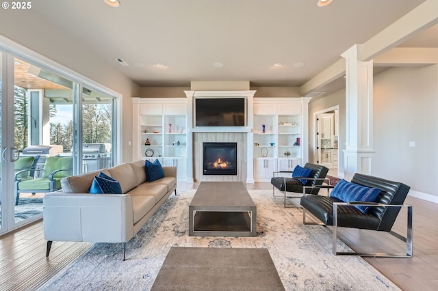 living area with recessed lighting, a glass covered fireplace, light wood-style floors, and decorative columns