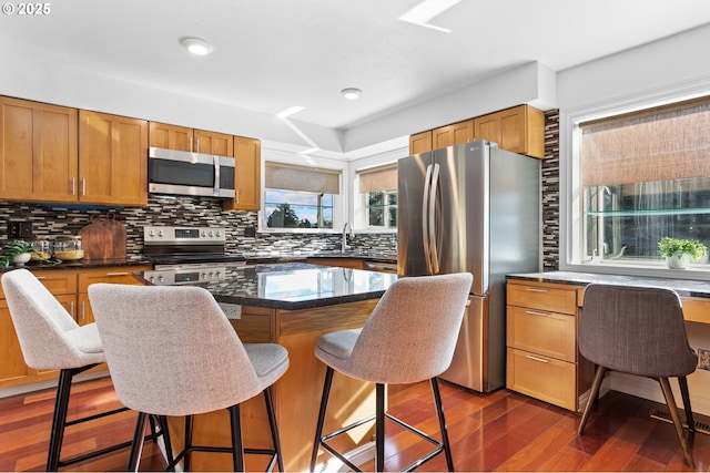 kitchen featuring a kitchen island, appliances with stainless steel finishes, backsplash, a kitchen breakfast bar, and dark wood-type flooring