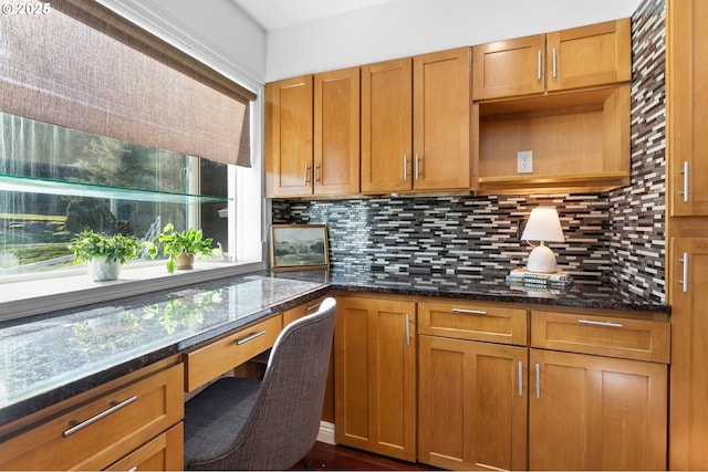 kitchen featuring tasteful backsplash, dark stone counters, and built in desk