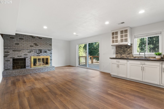 unfurnished living room featuring a healthy amount of sunlight, a brick fireplace, sink, and dark hardwood / wood-style floors