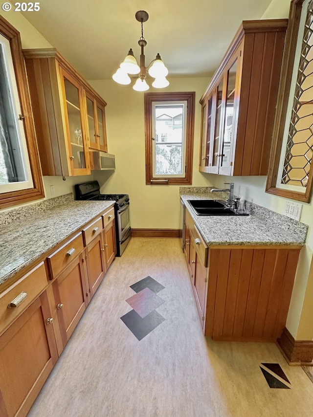 812 SW Saint Clair Ave Unit 3, Portland, OR 97205 - kitchen with gas stove, a sink, baseboards, brown cabinetry, and a chandelier