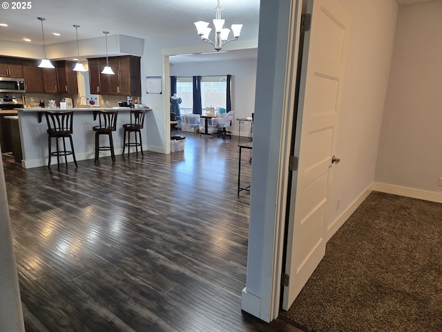 interior space featuring kitchen peninsula, a notable chandelier, tasteful backsplash, a breakfast bar area, and dark brown cabinets