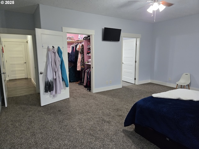 bedroom featuring a textured ceiling, a spacious closet, a closet, dark colored carpet, and ceiling fan