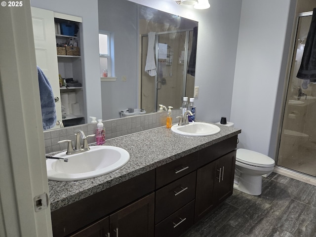 bathroom with wood-type flooring, toilet, vanity, a shower with shower door, and tasteful backsplash