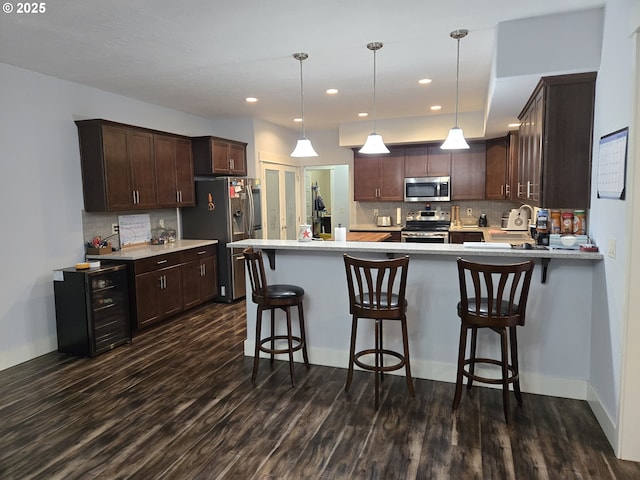 kitchen with stainless steel appliances, kitchen peninsula, hanging light fixtures, dark brown cabinetry, and dark wood-type flooring