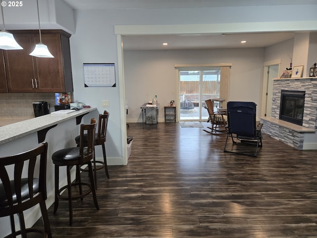 kitchen with decorative light fixtures, a fireplace, decorative backsplash, dark brown cabinets, and dark wood-type flooring