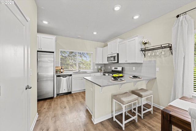 kitchen with stainless steel appliances, a peninsula, white cabinetry, light wood-style floors, and tasteful backsplash