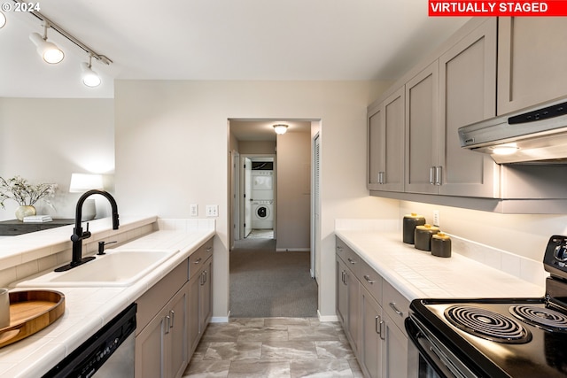 kitchen with black range with electric cooktop, stacked washer / drying machine, tile countertops, a sink, and under cabinet range hood