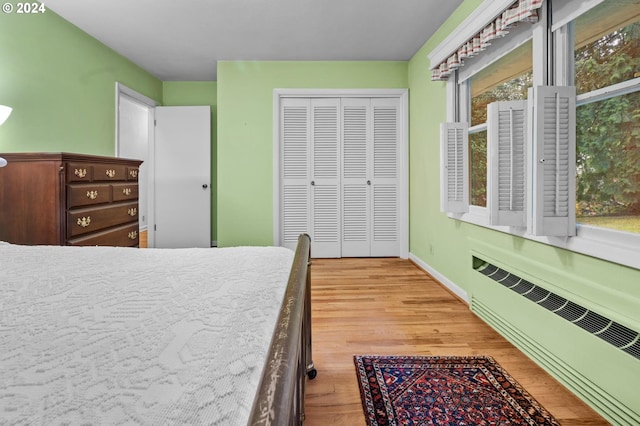 bedroom featuring multiple windows, radiator heating unit, light hardwood / wood-style floors, and a closet