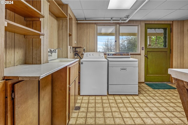 laundry room with cabinets, sink, wooden walls, and washing machine and clothes dryer