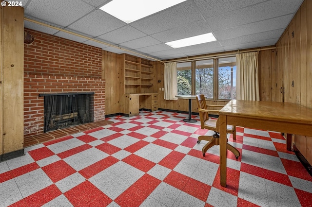 unfurnished office featuring a brick fireplace, a drop ceiling, and wooden walls