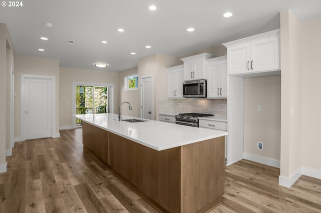 kitchen with decorative backsplash, an island with sink, stainless steel appliances, white cabinetry, and a sink