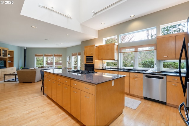 kitchen featuring a center island, light wood-style flooring, dark stone countertops, a towering ceiling, and stainless steel appliances