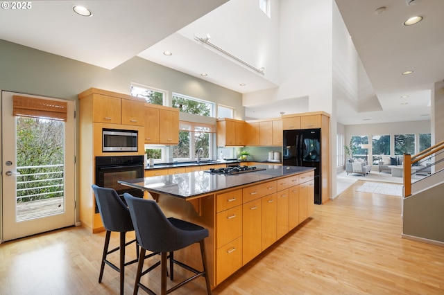 kitchen featuring light wood finished floors, a center island, a kitchen bar, a high ceiling, and black appliances