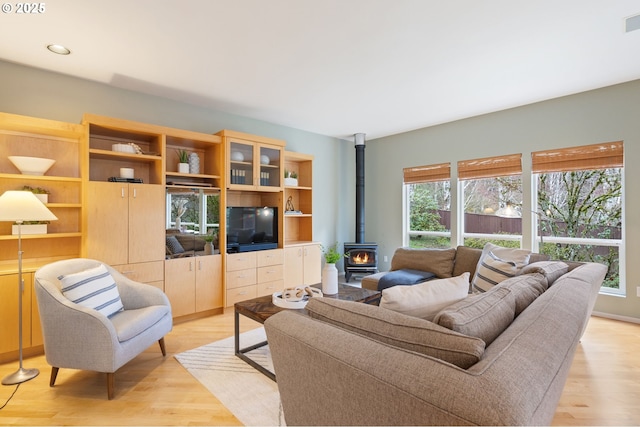 living room with plenty of natural light, visible vents, a wood stove, and light wood-style floors