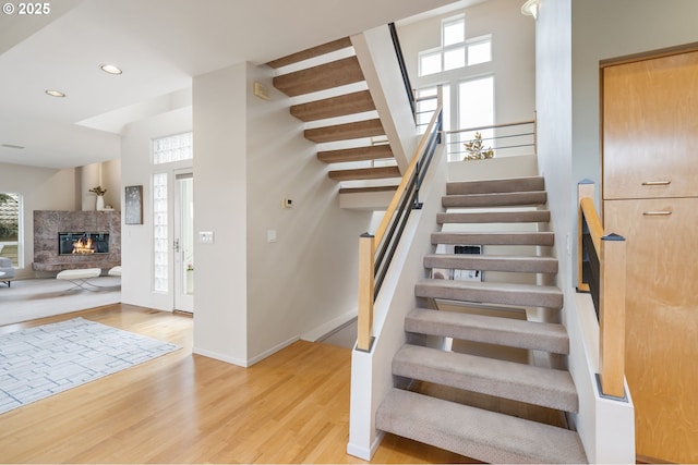 staircase with a glass covered fireplace, recessed lighting, baseboards, and wood finished floors