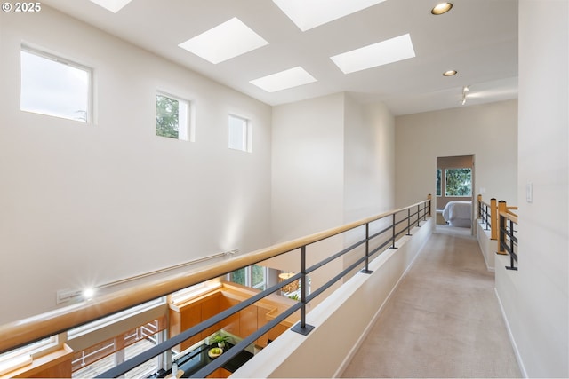 corridor featuring light colored carpet, an upstairs landing, plenty of natural light, and a skylight