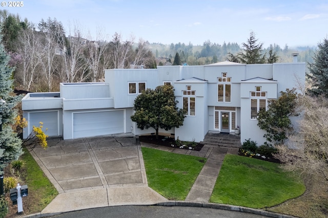 art deco home with a front yard, a garage, driveway, and stucco siding