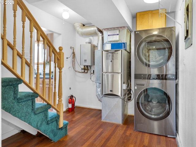 laundry area featuring cabinet space, water heater, stacked washer / drying machine, and wood finished floors