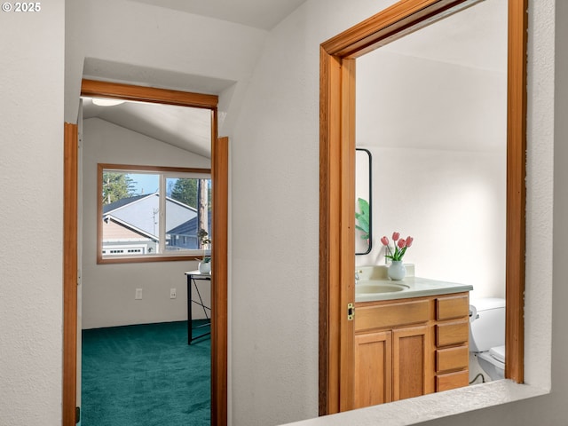 hallway featuring a sink, vaulted ceiling, and carpet flooring