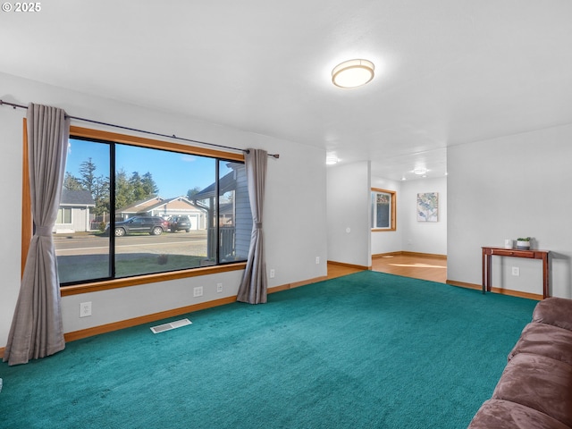 unfurnished living room featuring baseboards, visible vents, and carpet flooring